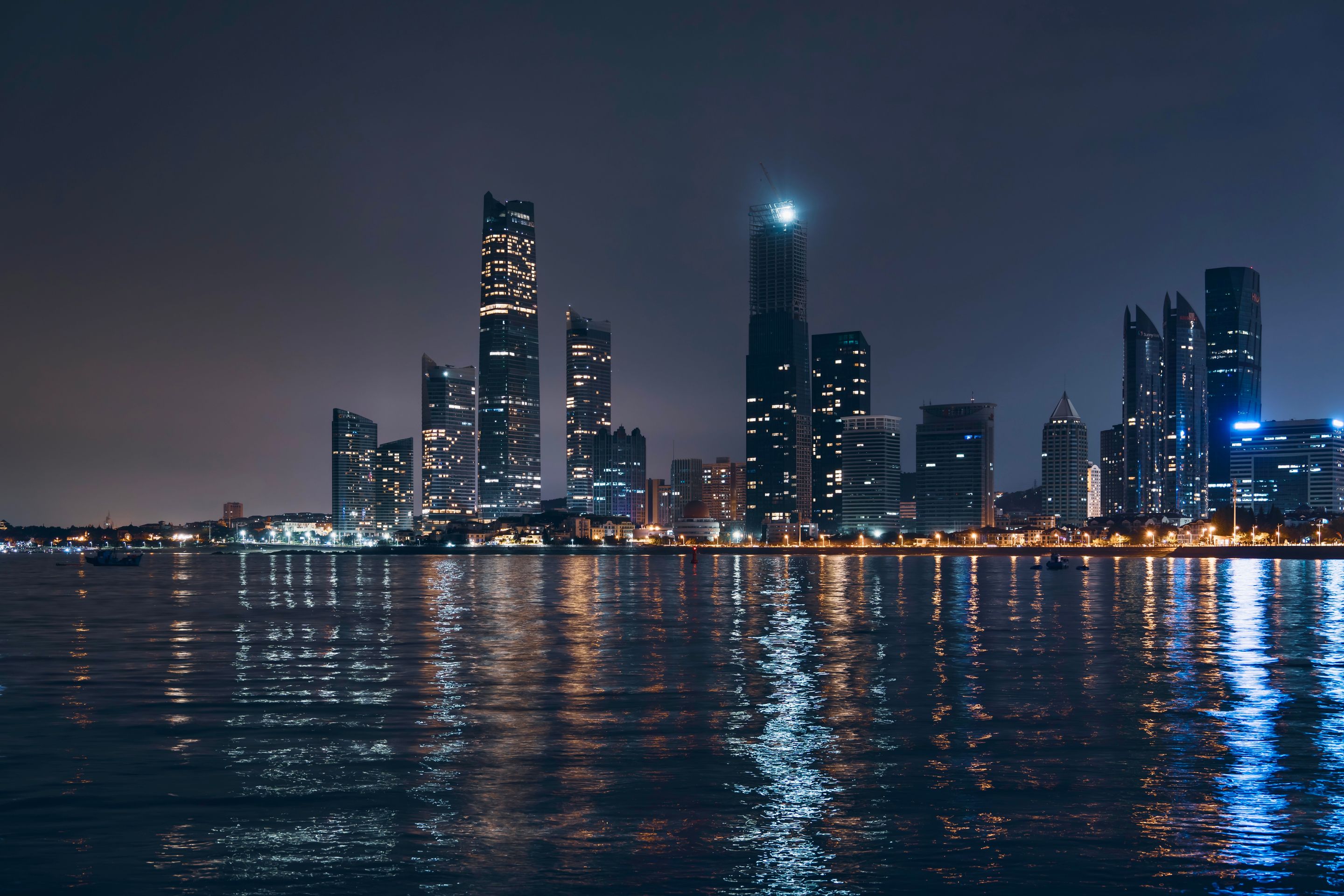 Night view of Abu Dhabi skyline with reflections on water, showcasing modern architecture.