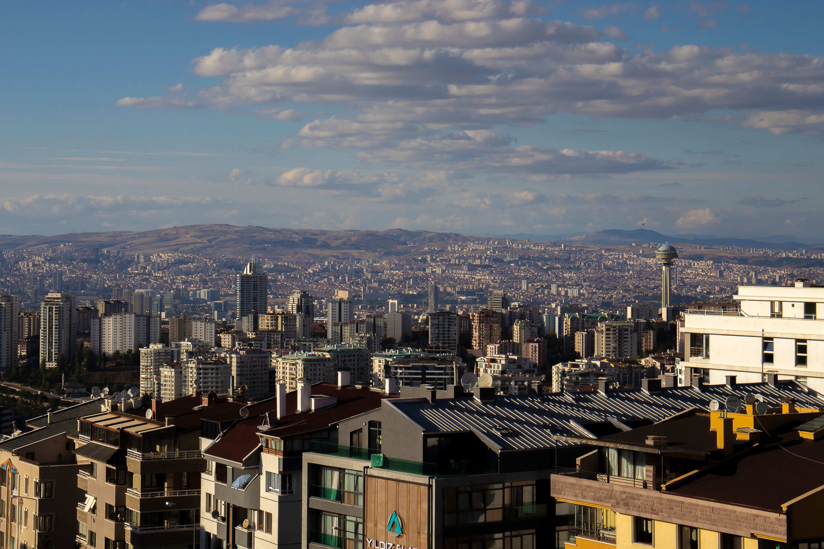 A sweeping aerial view of Ankara's cityscape under a bright, cloudy sky.