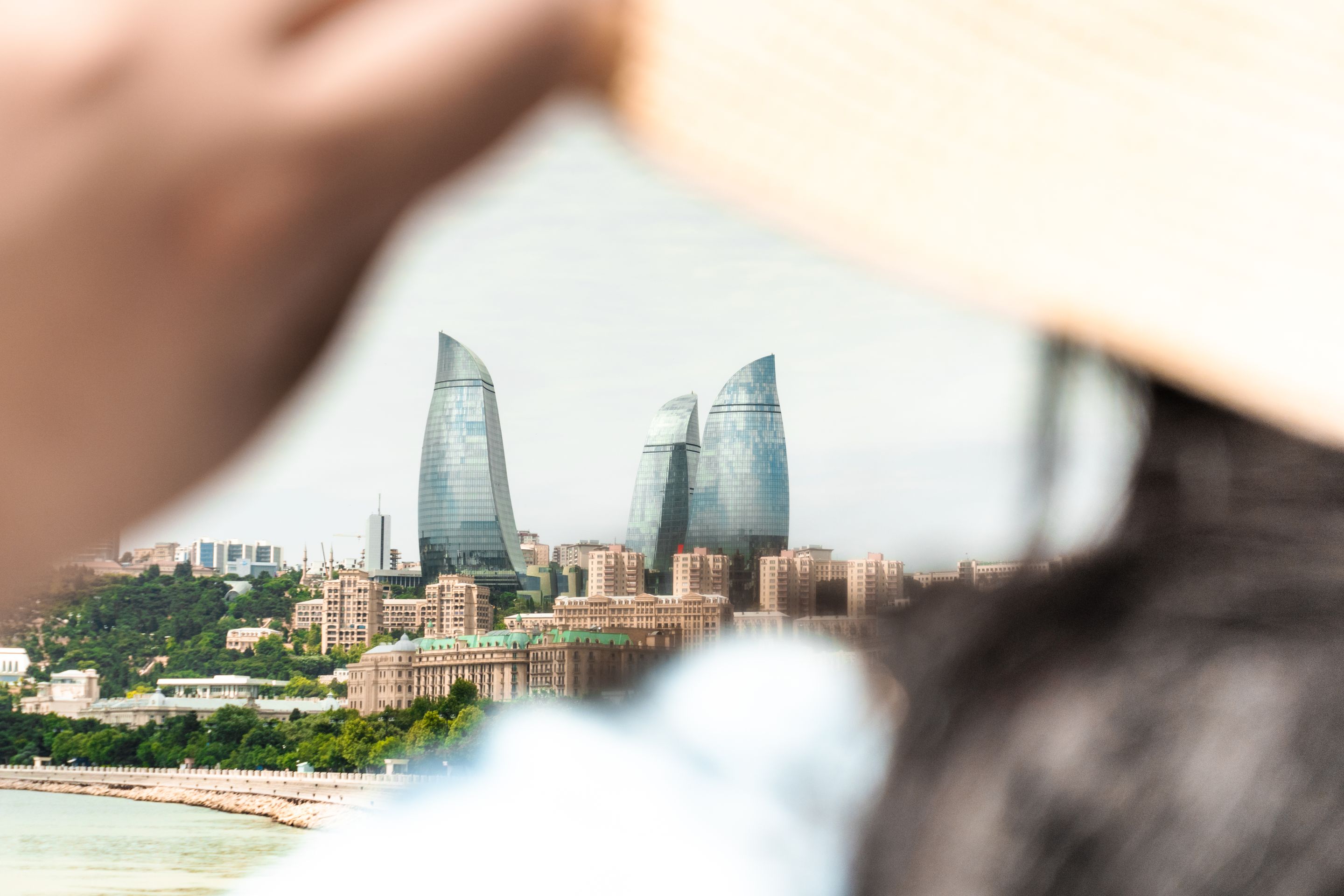 A scenic view of Baku's iconic Flame Towers seen through the perspective of a person adjusting a sunhat.