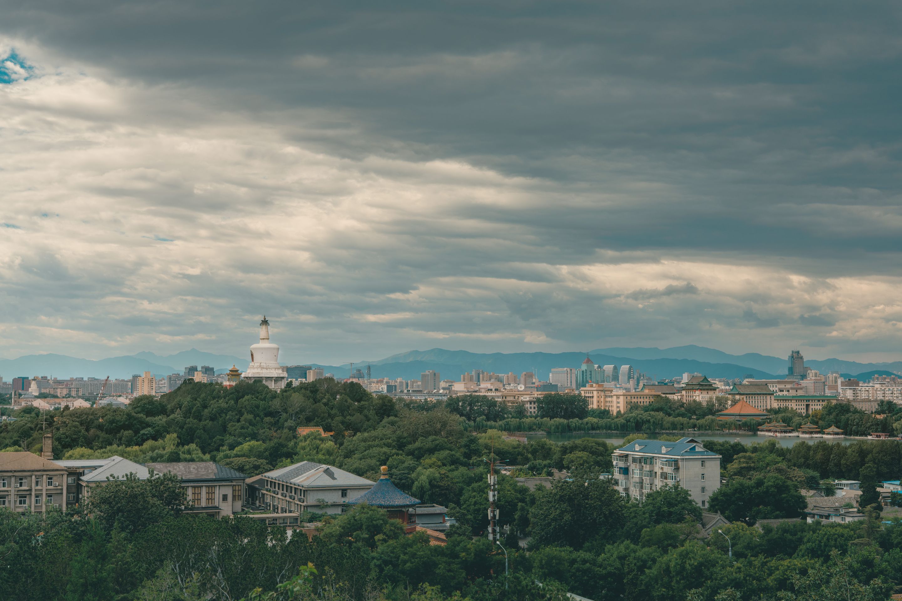 Panoramic view of Beijing with the iconic White Dagoba stupa under a cloudy sky.