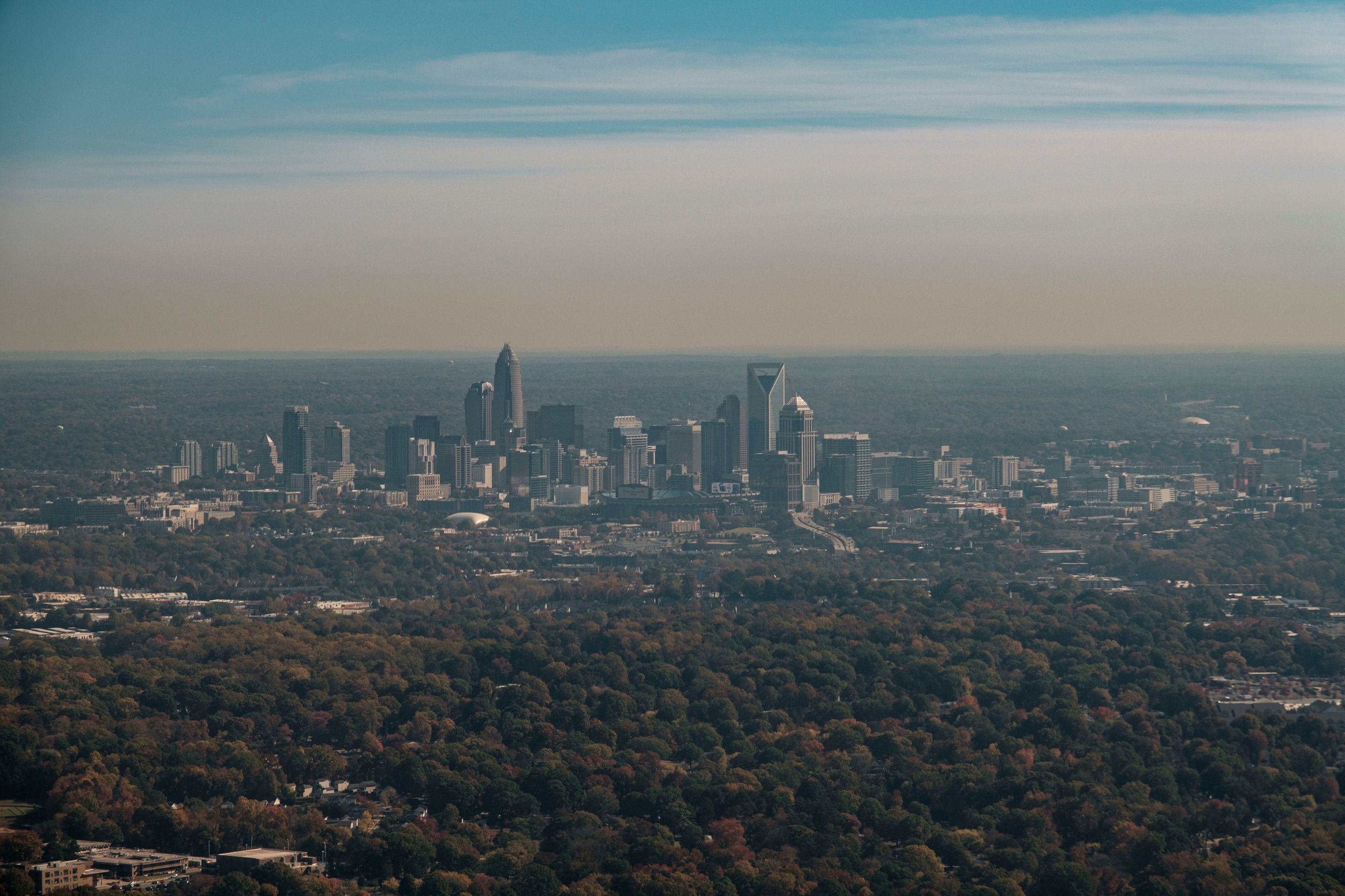 Stunning aerial shot of Charlotte skyline surrounded by fall foliage under a clear sky.