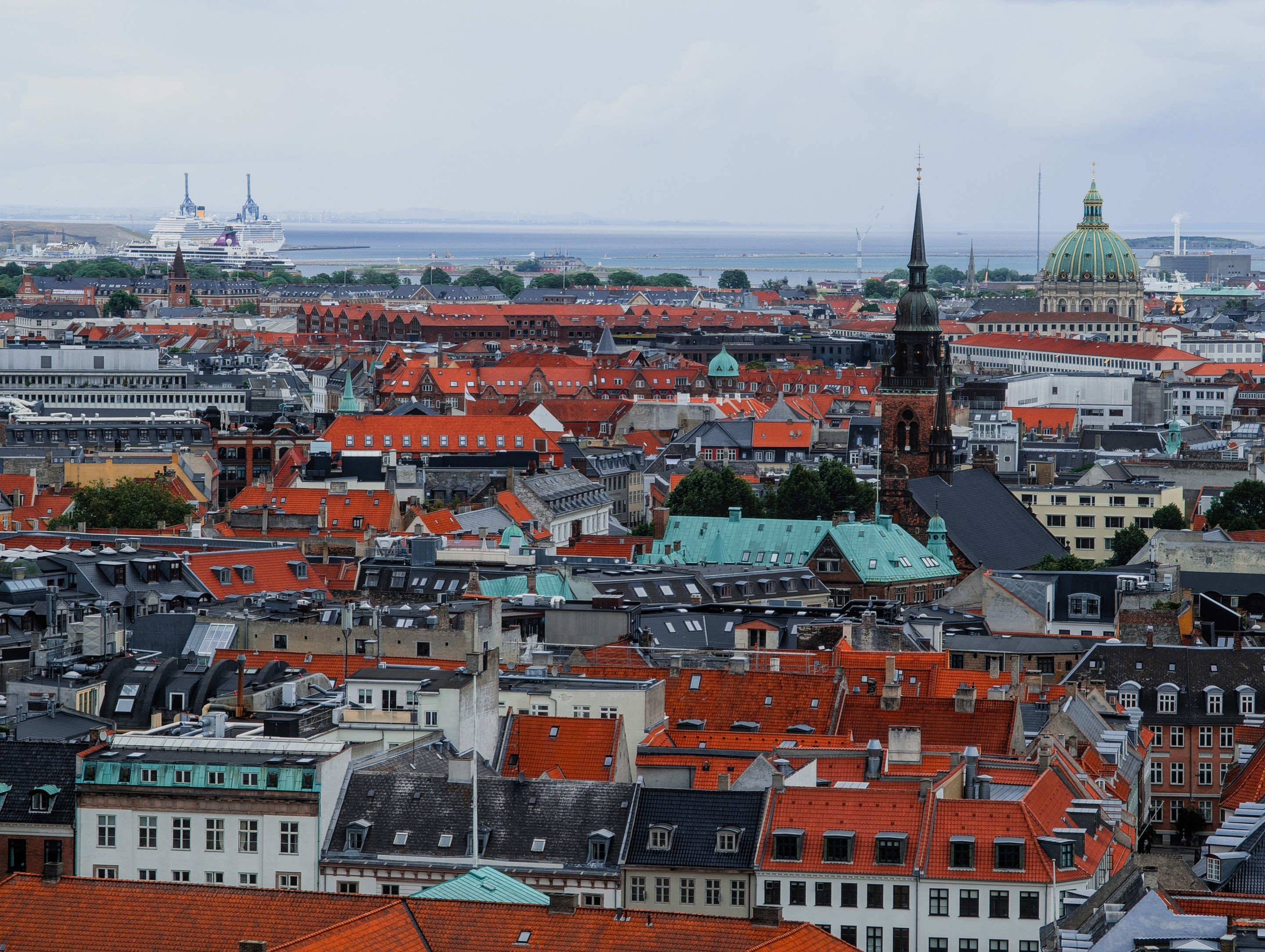 A panoramic view of Copenhagen's rooftops with iconic architecture and a distant harbor.
