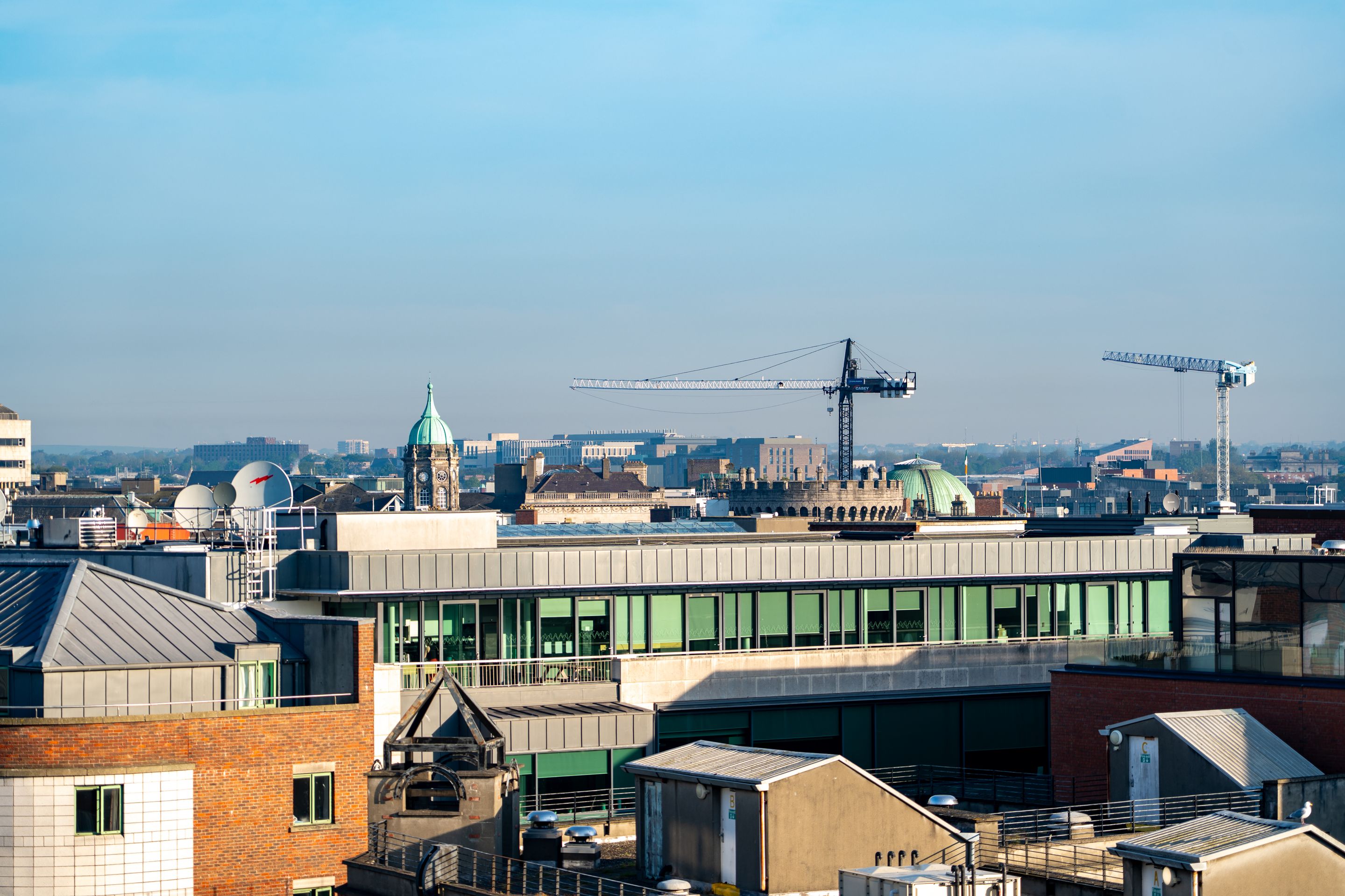 A vibrant view of Dublin's cityscape featuring construction cranes and iconic architecture under a clear blue sky.