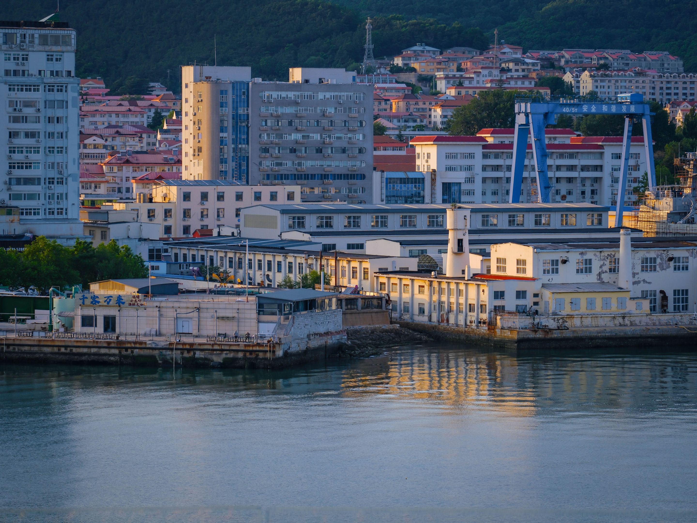 A scenic view of city buildings and industrial structures along a calm waterfront during dusk.