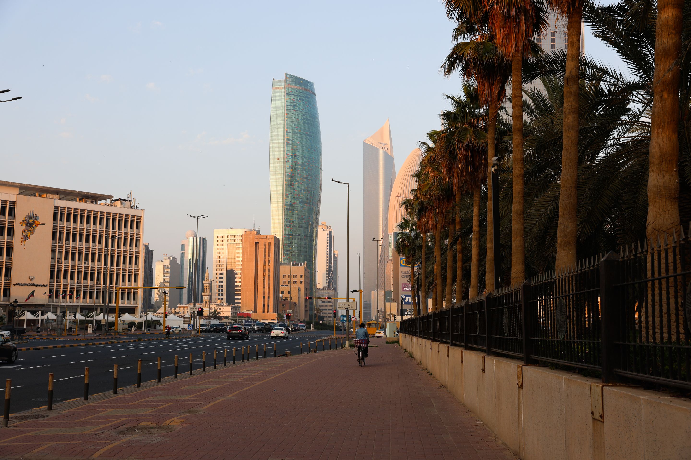 Scenic view of Kuwait City's architecture with skyscrapers and palm trees under a clear sky.