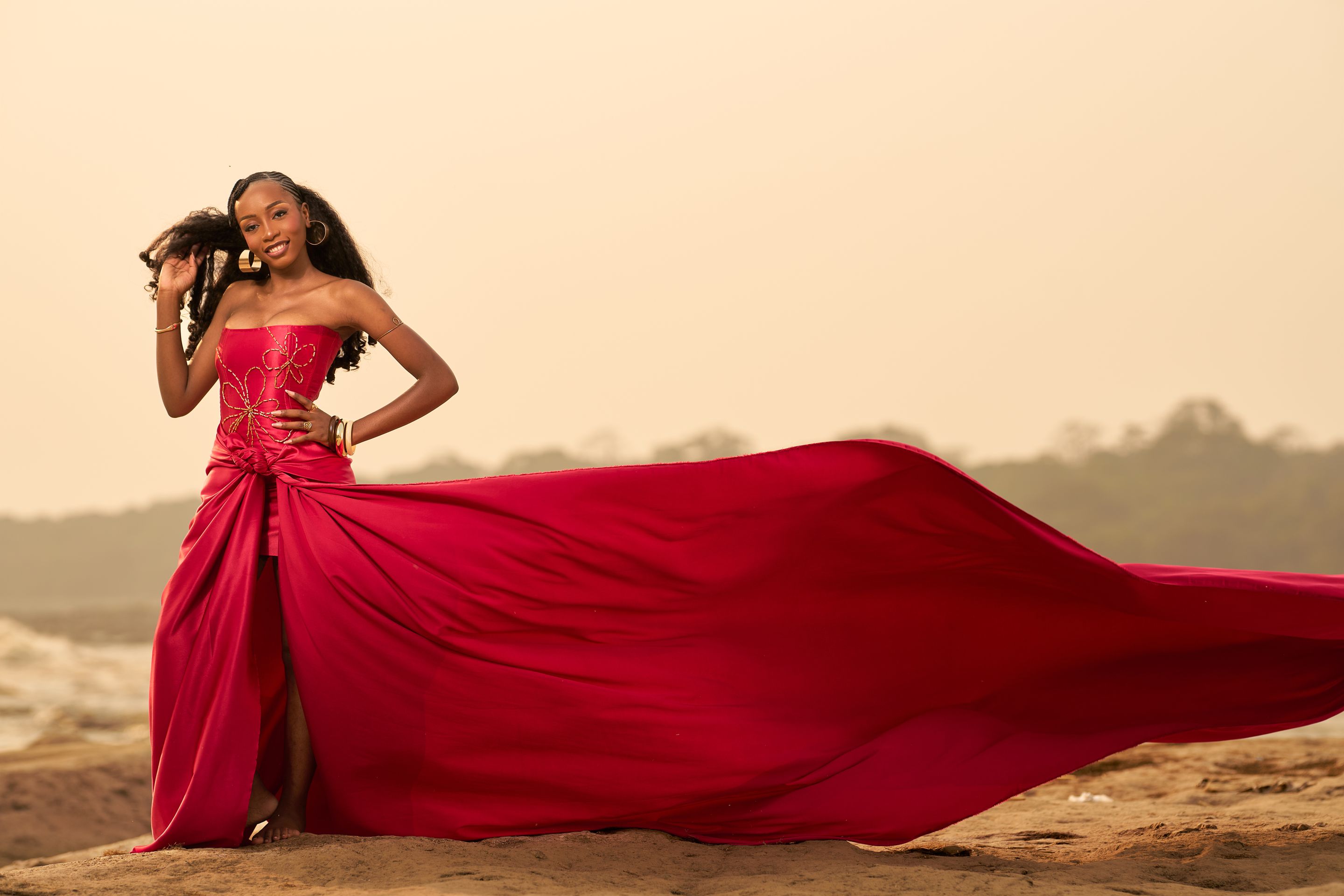 Woman in a stunning red dress posing gracefully on a sandy beach during day.