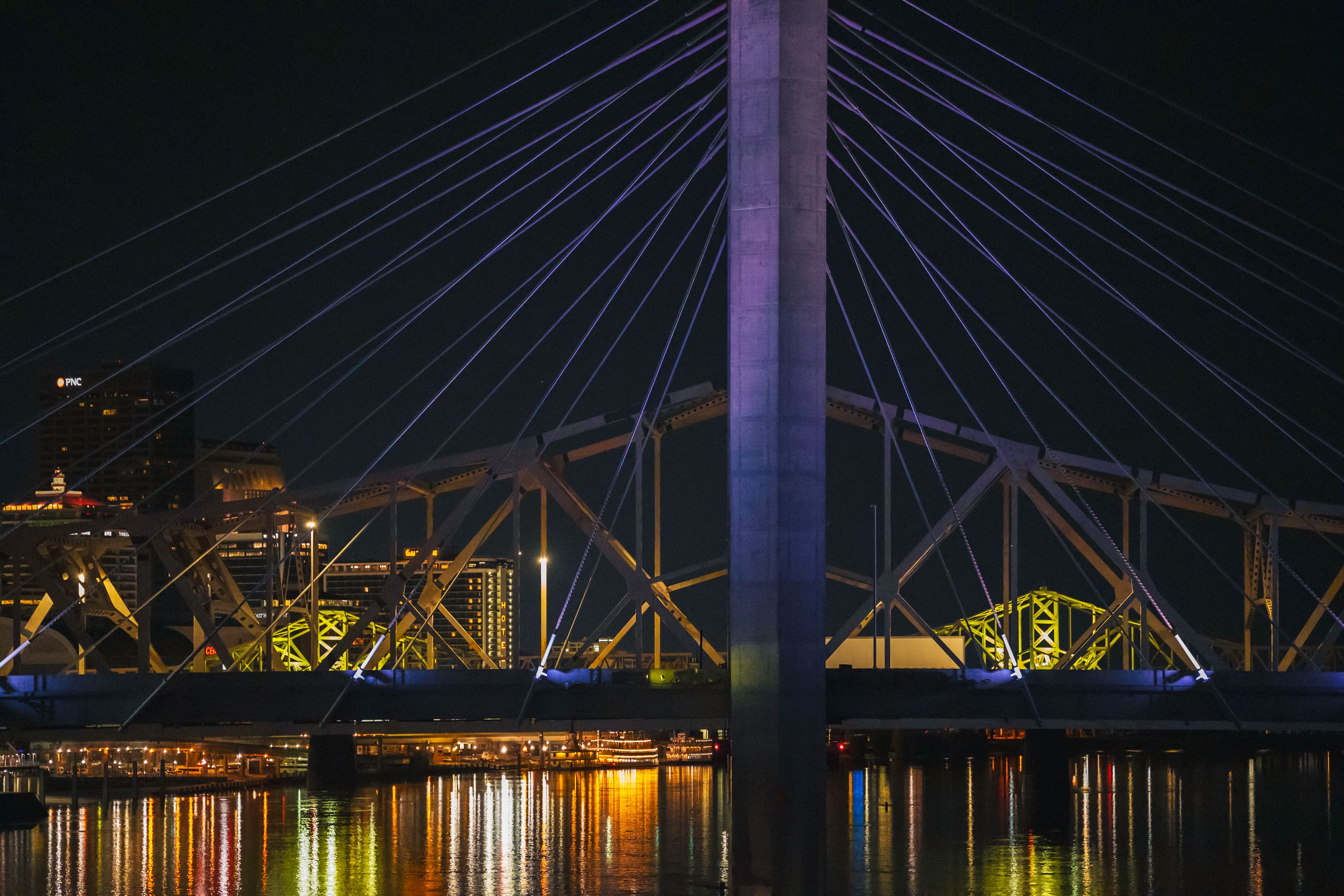 A vibrant night scene of a cable-stayed bridge in Kentucky with city lights reflecting on the water.