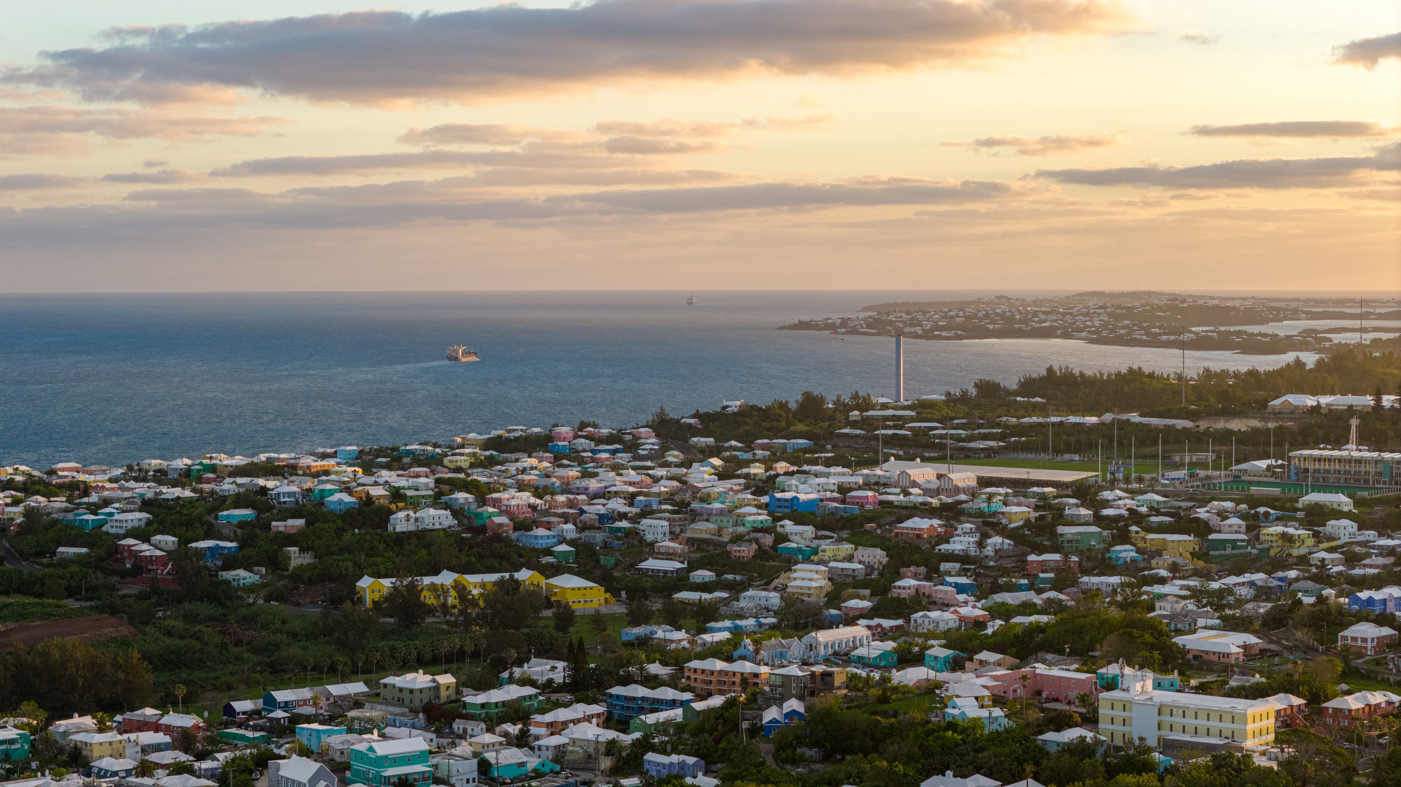 Stunning aerial view of Bermuda's coastal town with vibrant houses and ocean at sunset.