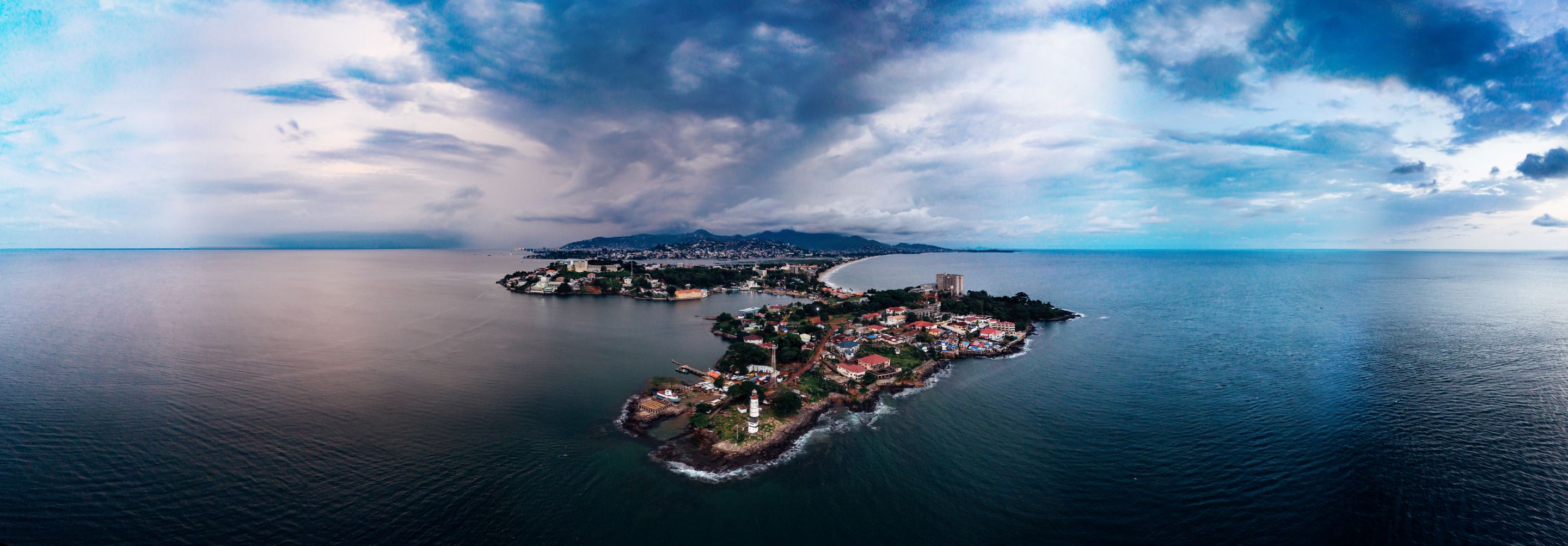 Breathtaking aerial view of a coastal island surrounded by the vast blue ocean under a dramatic sky.