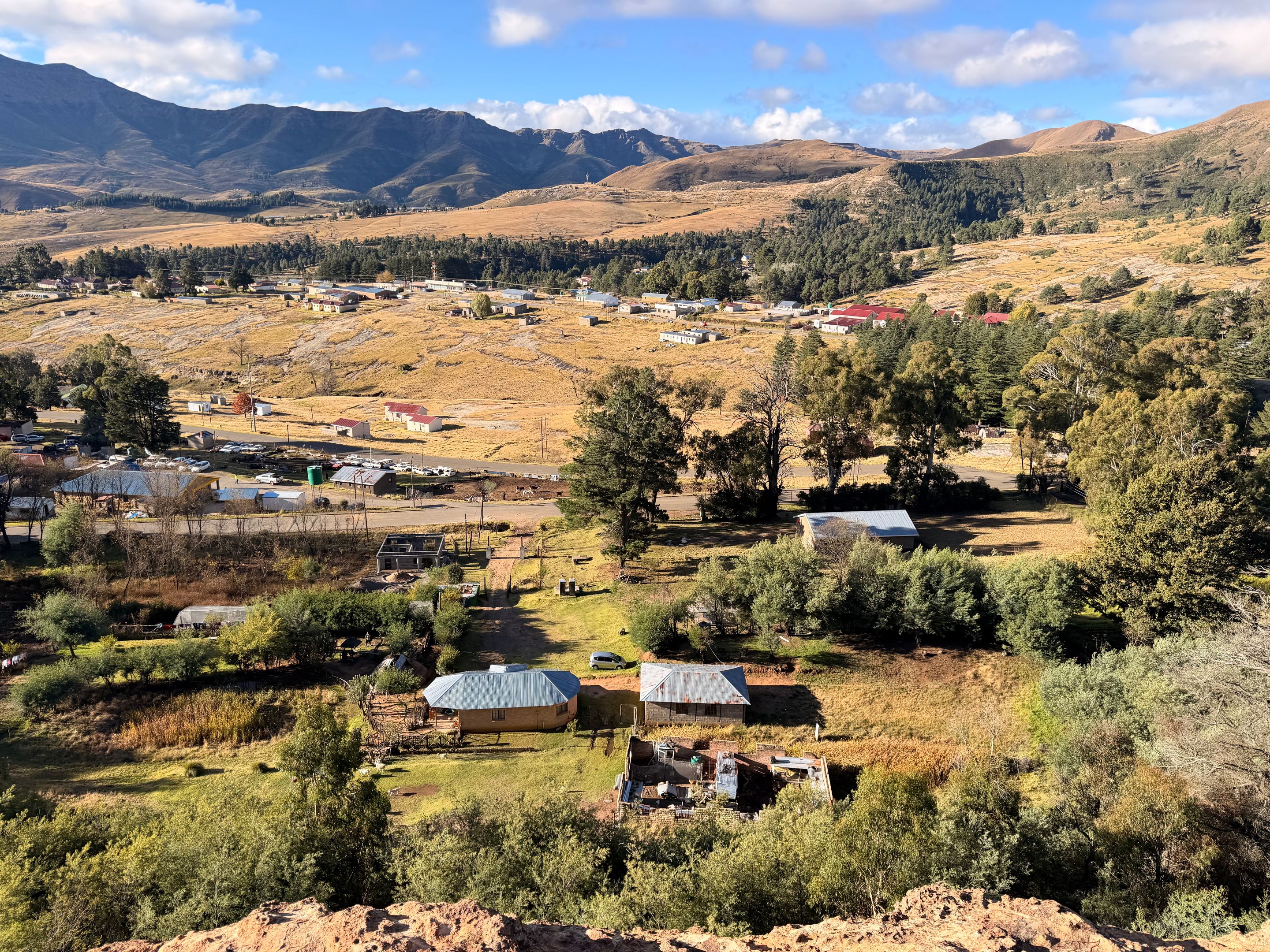 A picturesque aerial view of a rural village in Lesotho, surrounded by mountains and lush greenery.