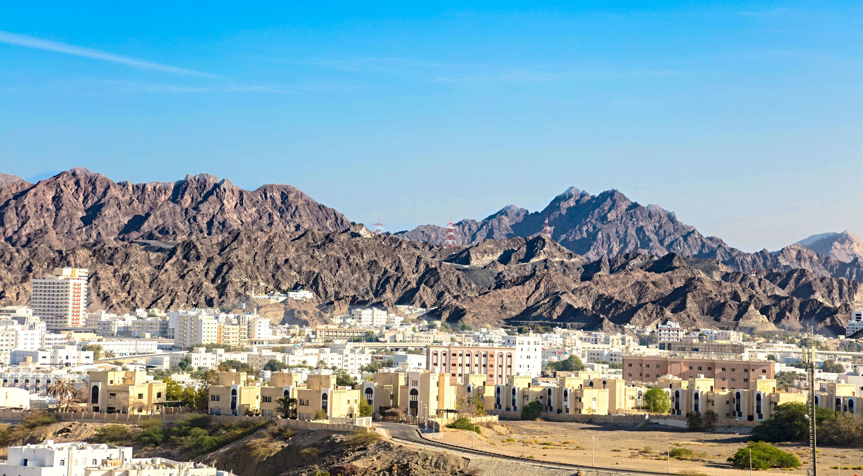 A vibrant city nestled against rugged mountains under a clear blue sky.