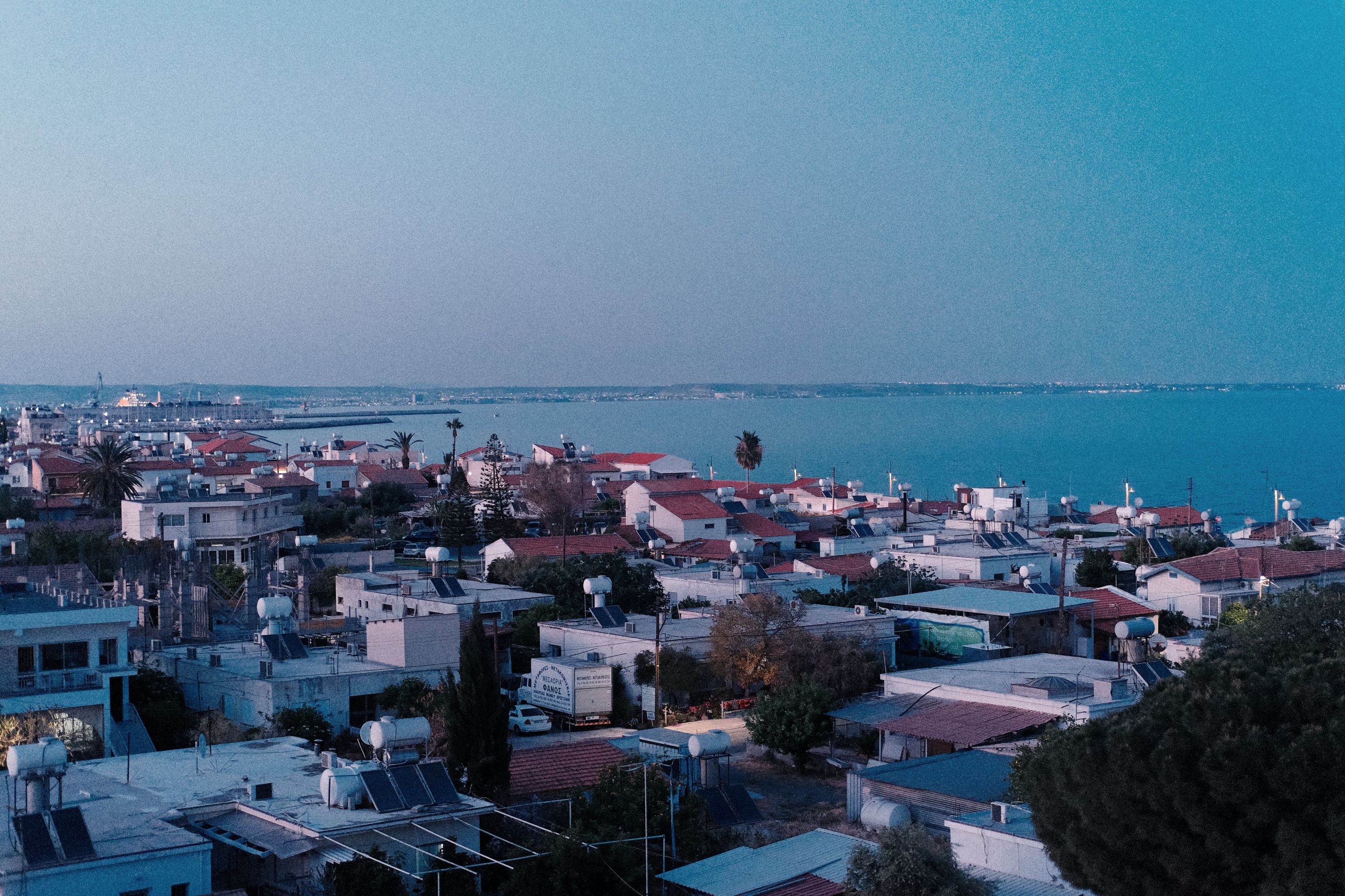 Aerial view of Larnaca's rooftops leading to a serene sea horizon at sunset.
