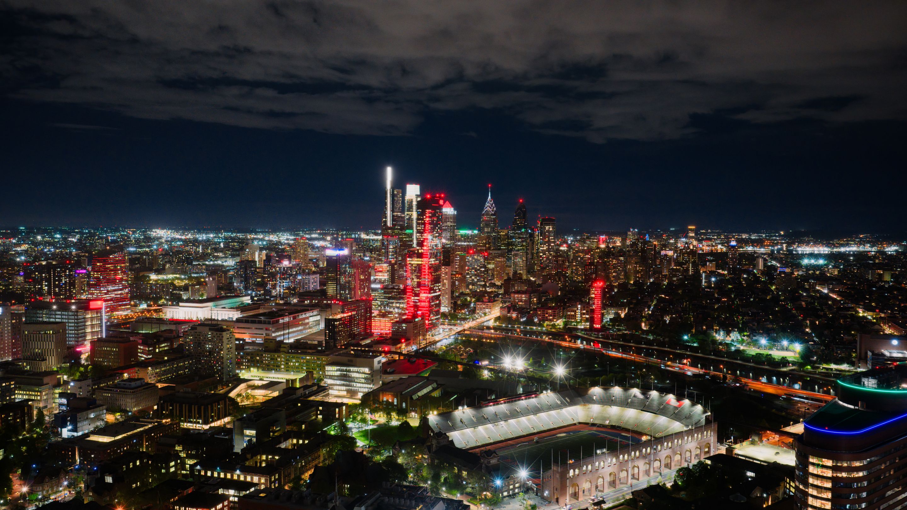A breathtaking aerial view of Philadelphia's illuminated skyline at night, highlighting the vibrant cityscape and a prominent stadium.
