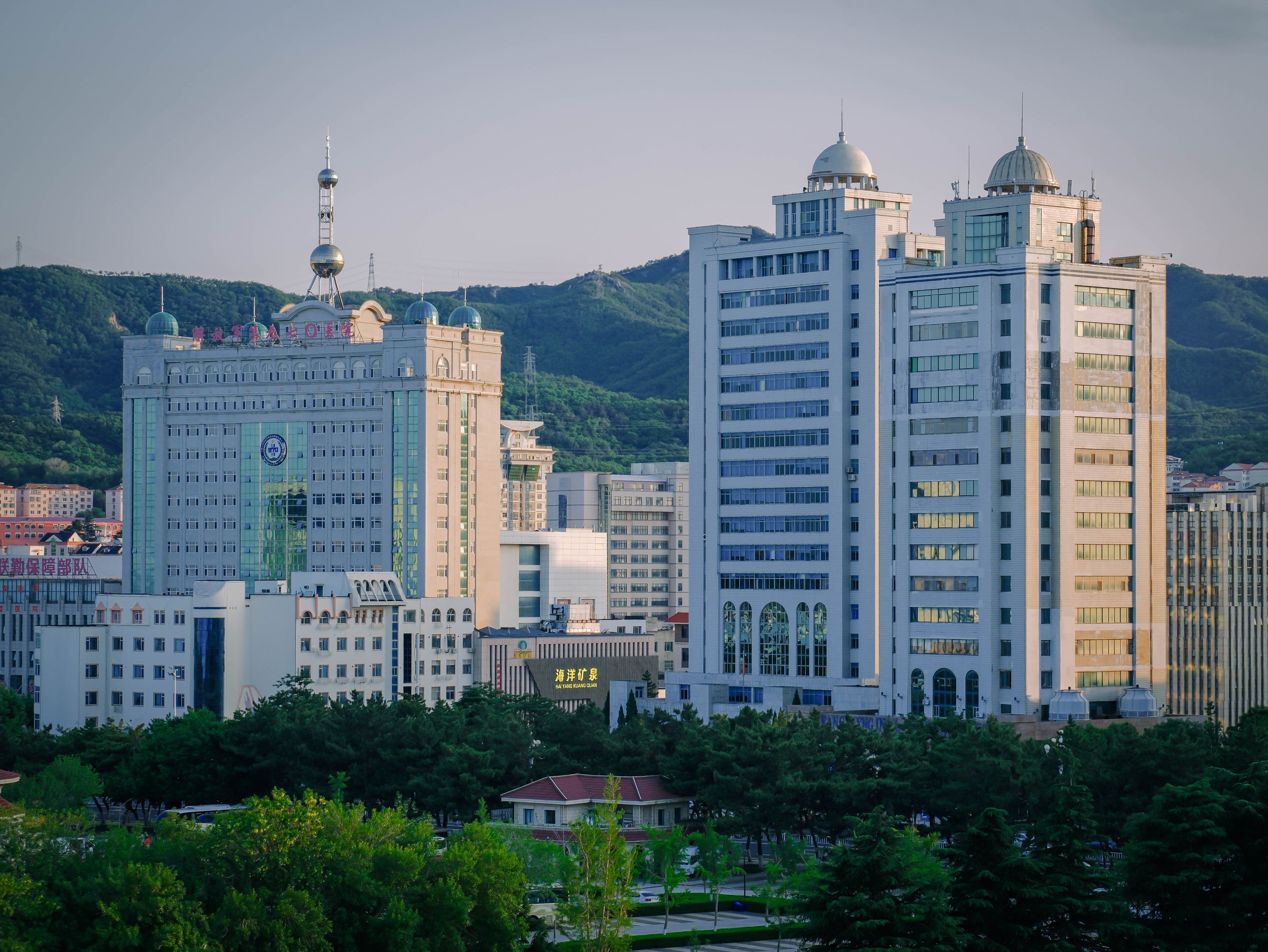 Urban cityscape with modern high-rise buildings and lush greenery at dusk.