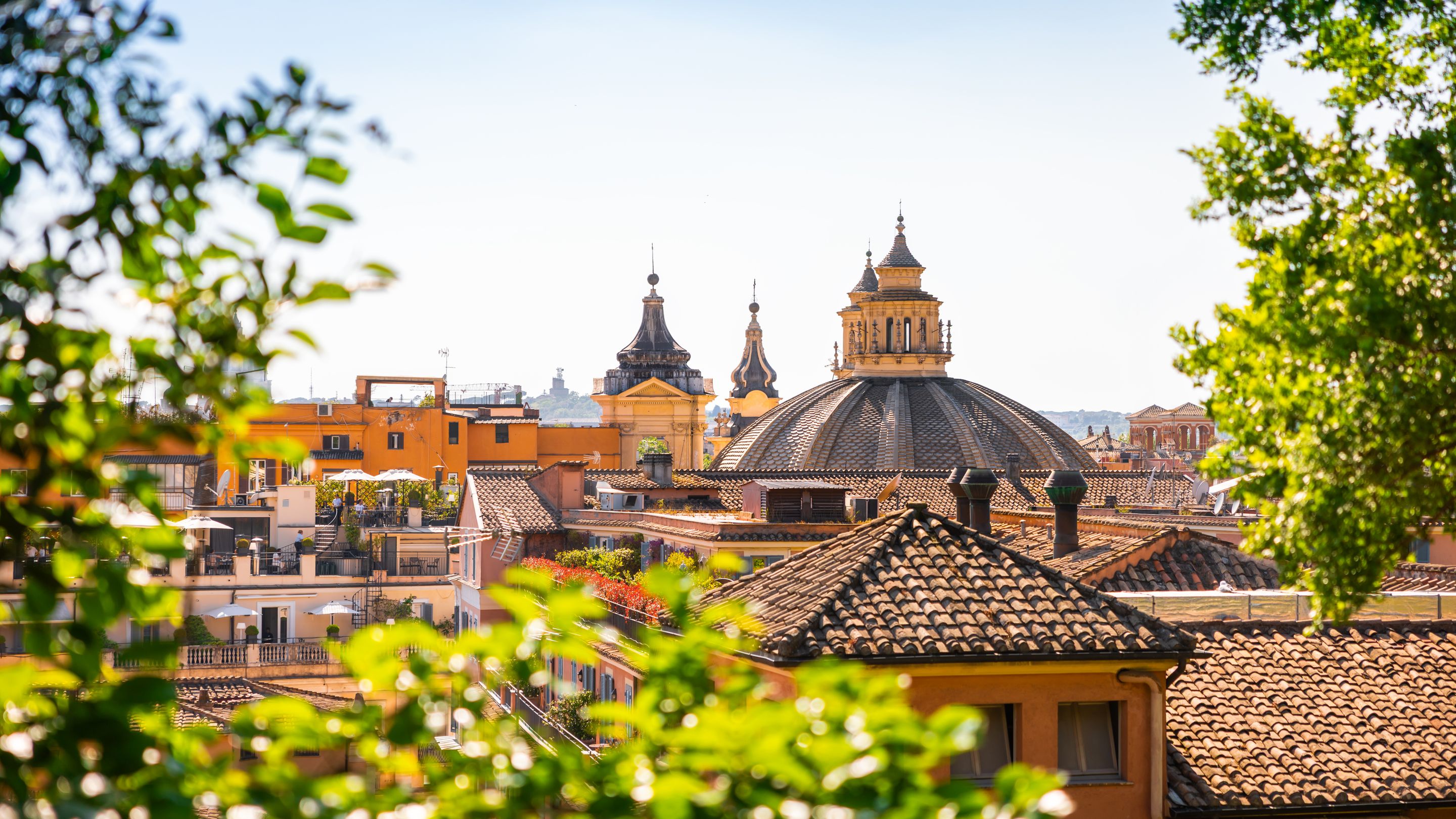 Beautiful skyline of Rome's historic rooftops with lush greenery framing the scene.