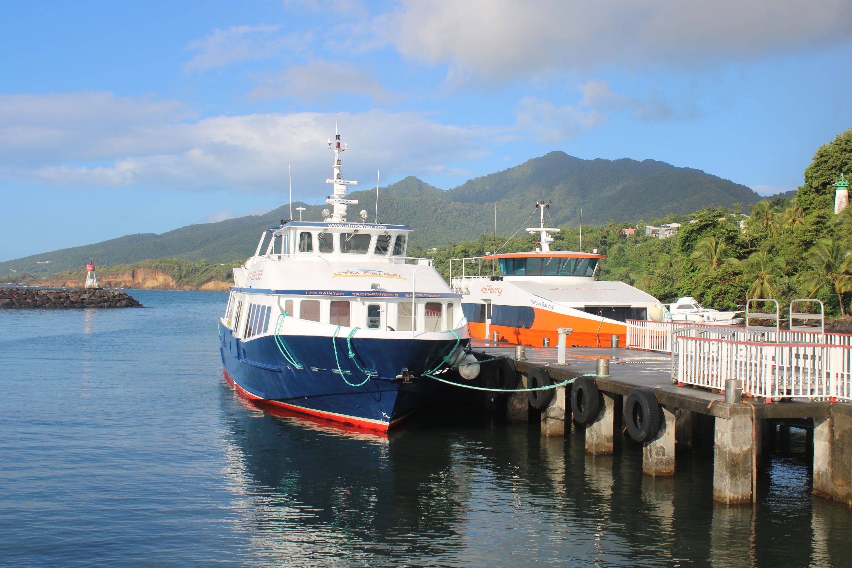 Ferry boats at a scenic tropical harbor with mountains in the background.