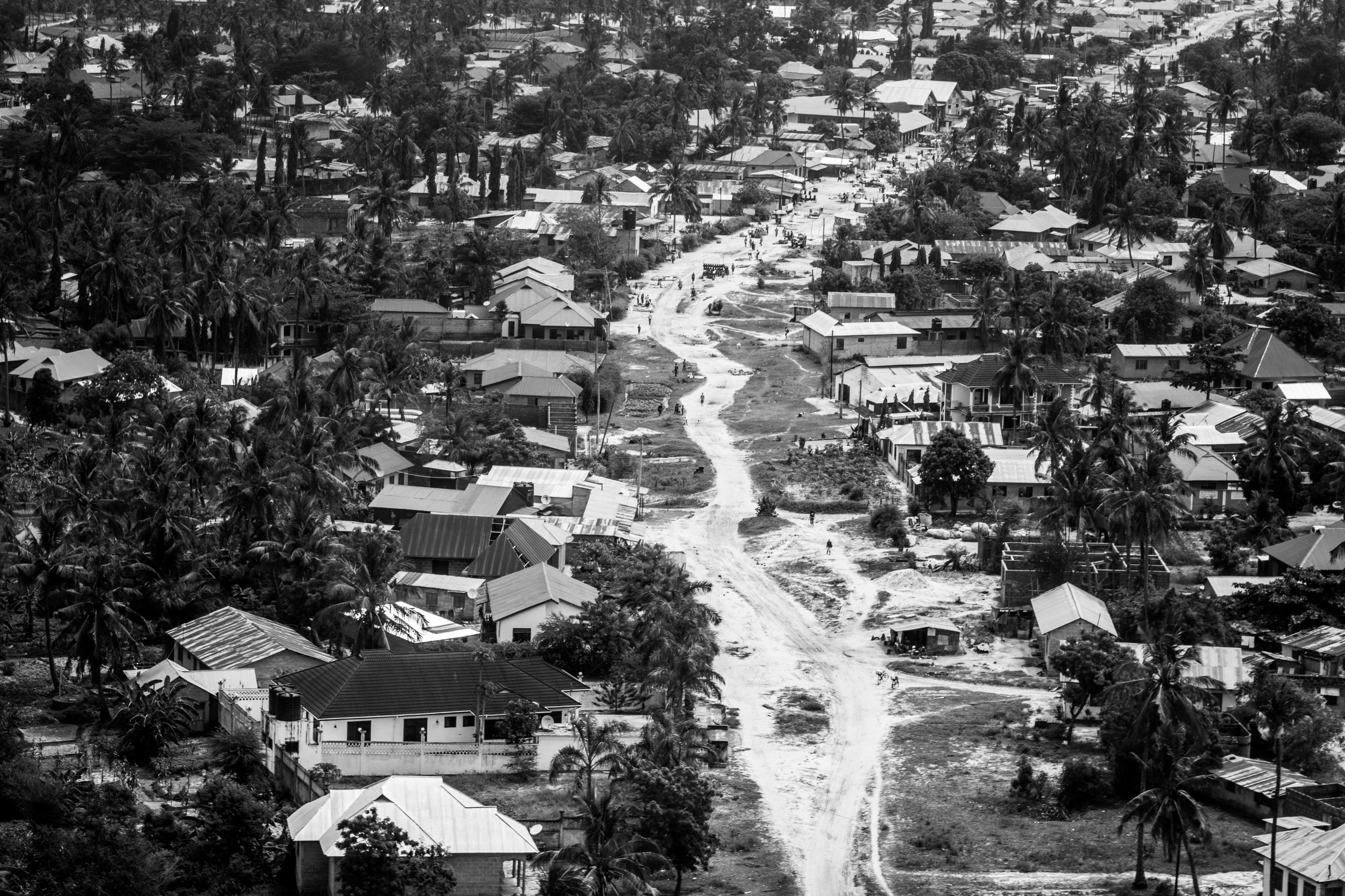 Black and white aerial view of a Tanzanian suburb with houses and unpaved roads.