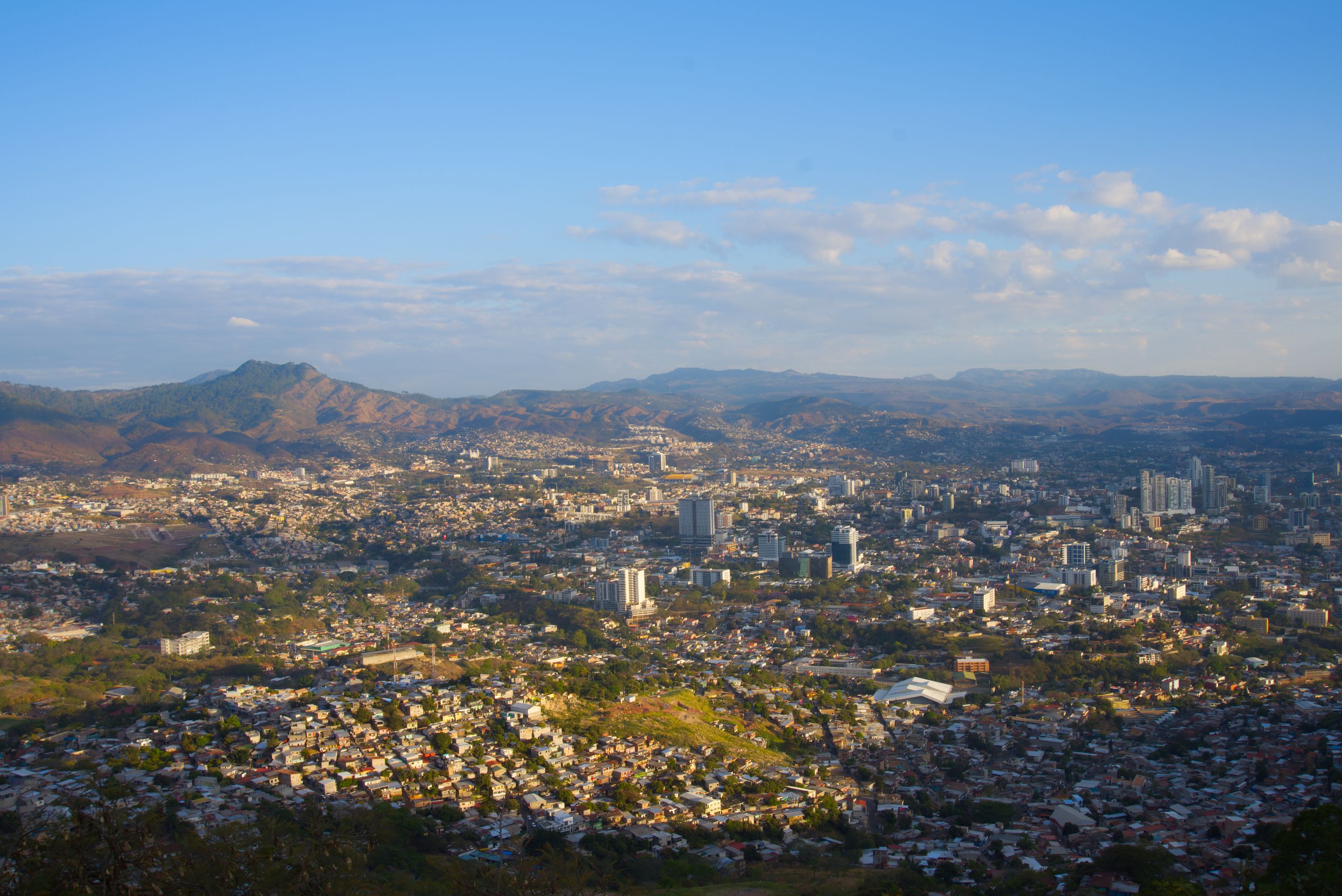 Aerial view of Tegucigalpa city with mountain backdrop under a clear blue sky.