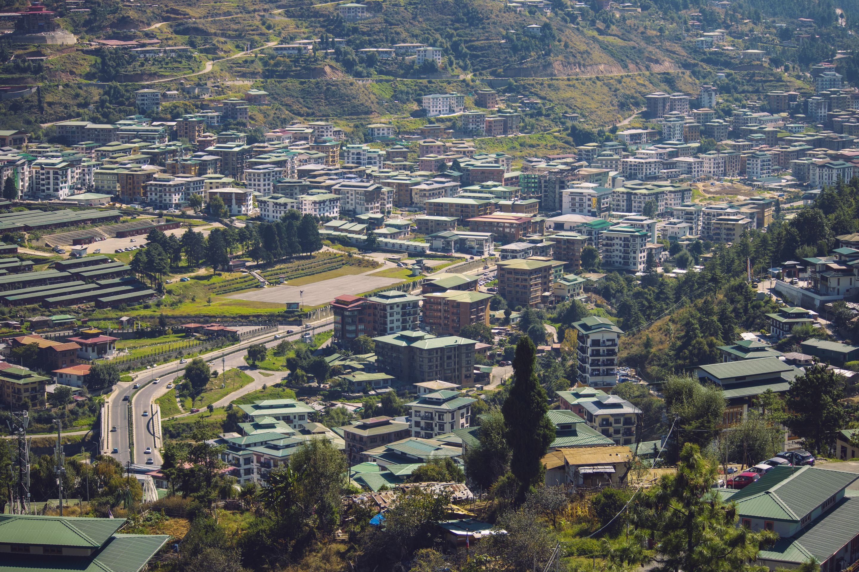 Explore the vibrant cityscape of Thimphu, Bhutan, with dense buildings nestled in lush hills.