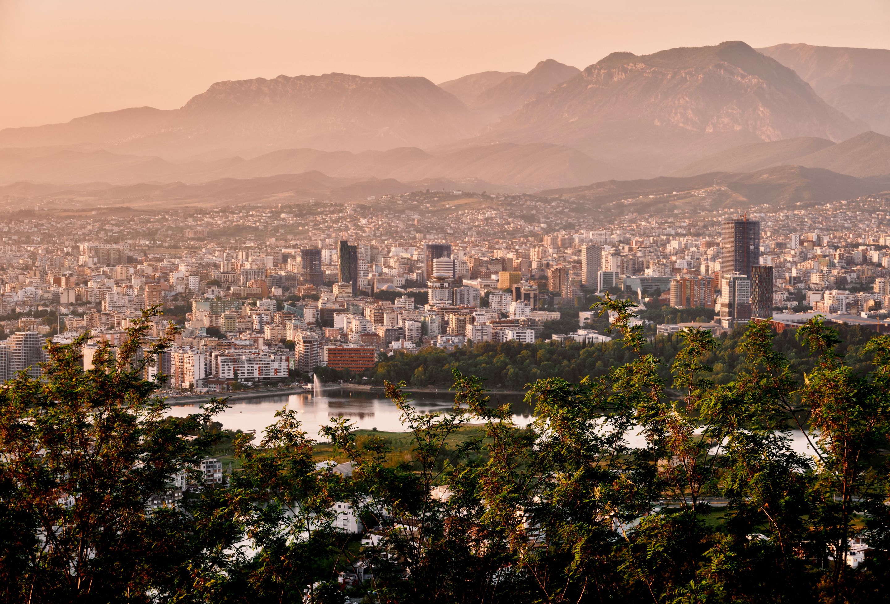A stunning aerial view of Tirana's skyline framed by mountains and lush greenery during sunset.