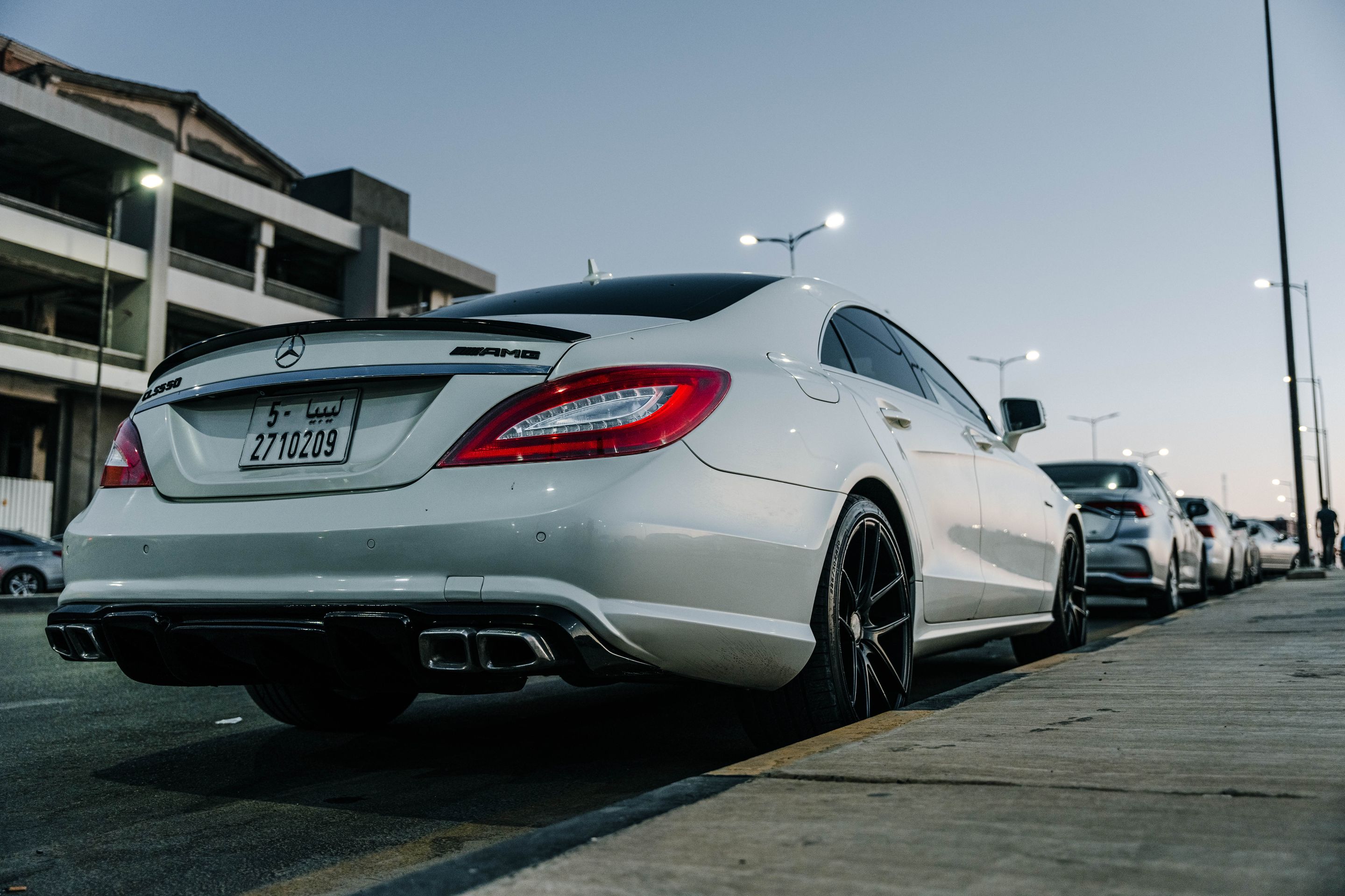 White Mercedes Benz CLS parked on an urban street in Tripoli, showcasing sleek design against a twilight backdrop.