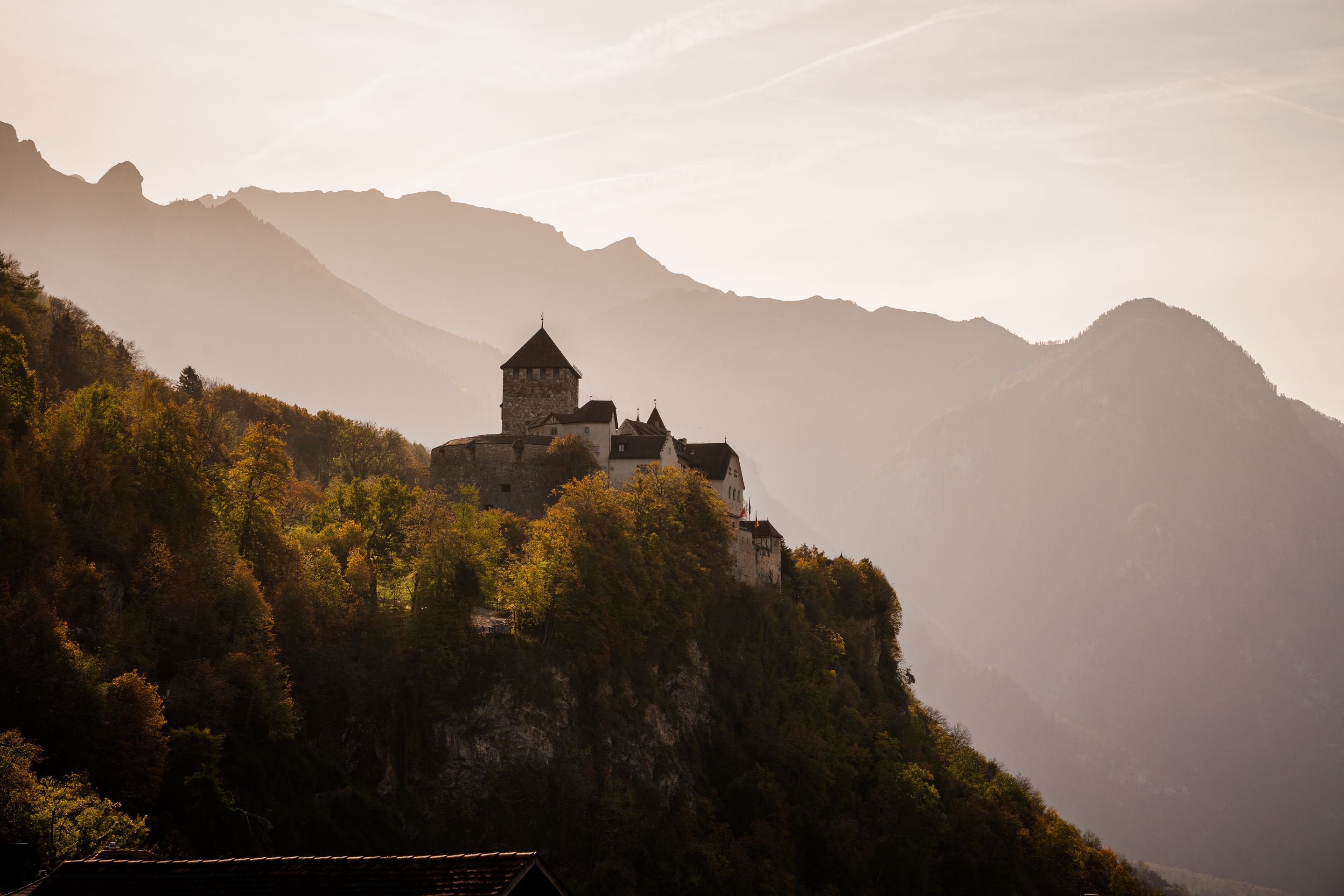 Stunning view of a medieval castle in Vaduz, surrounded by autumnal mountains.