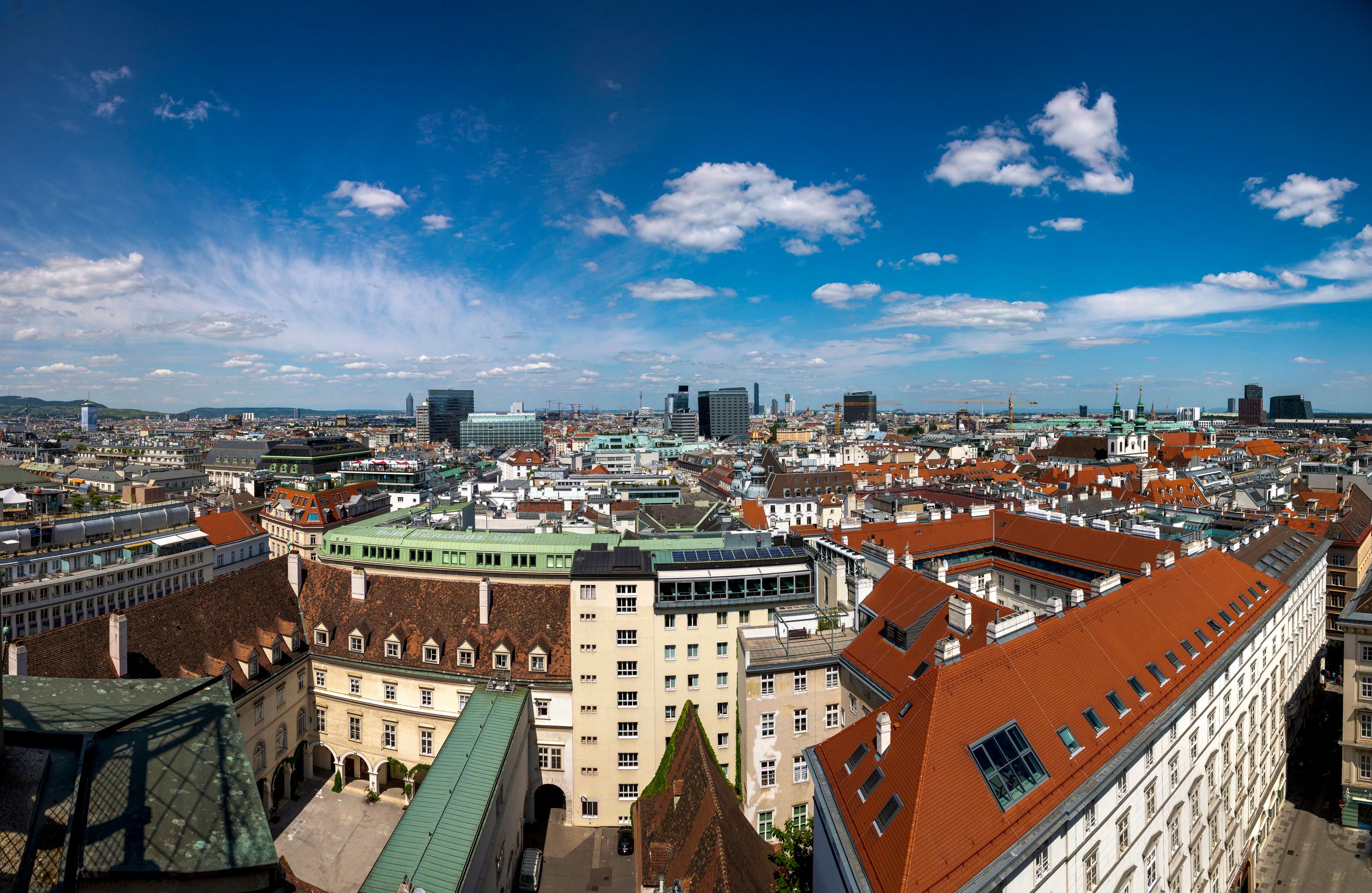Wide-angle view of Vienna skyline featuring mix of historical and modern architecture under a bright blue sky.