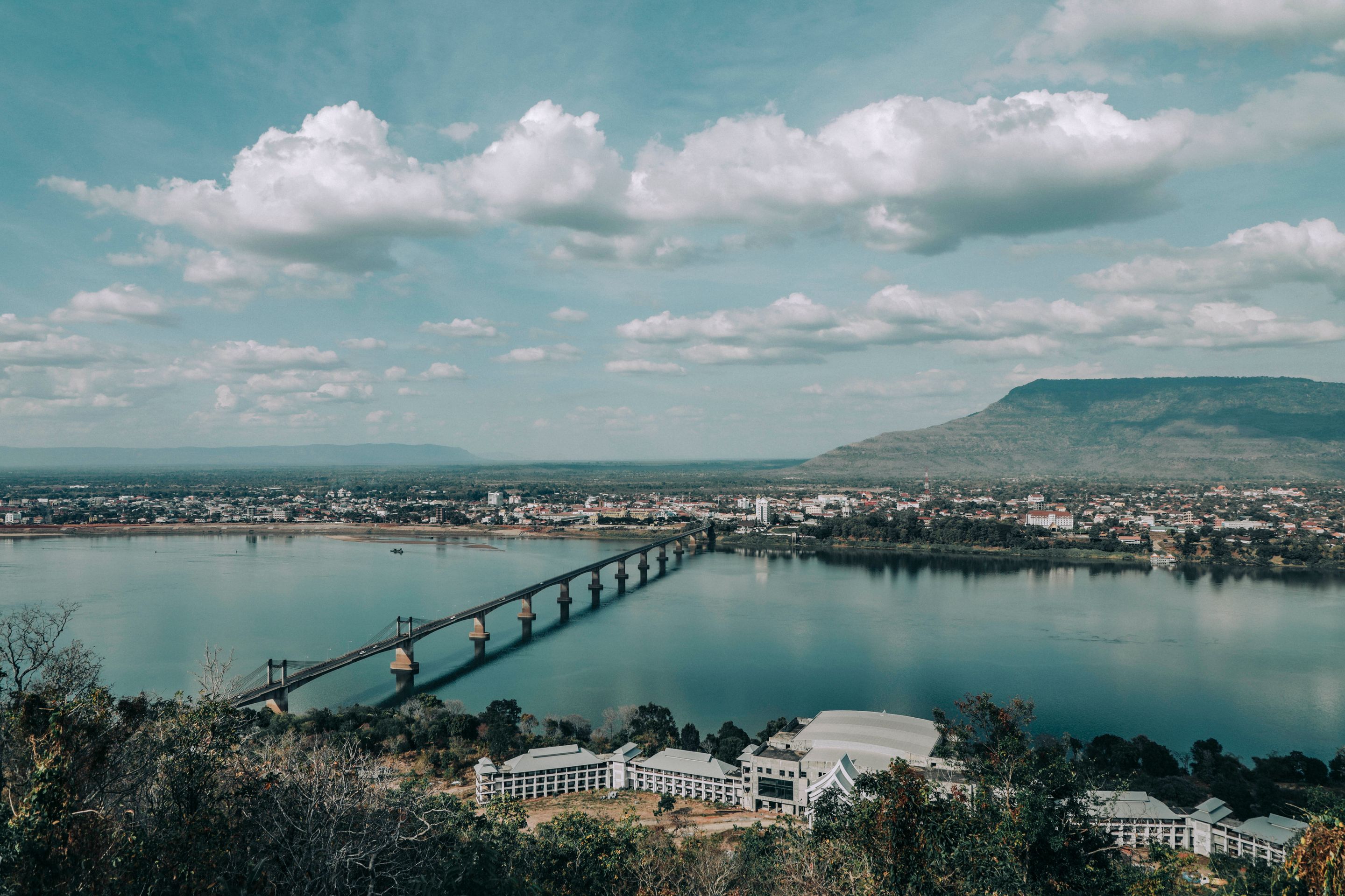 A picturesque bridge spans the Mekong River in a tranquil Laotian landscape.