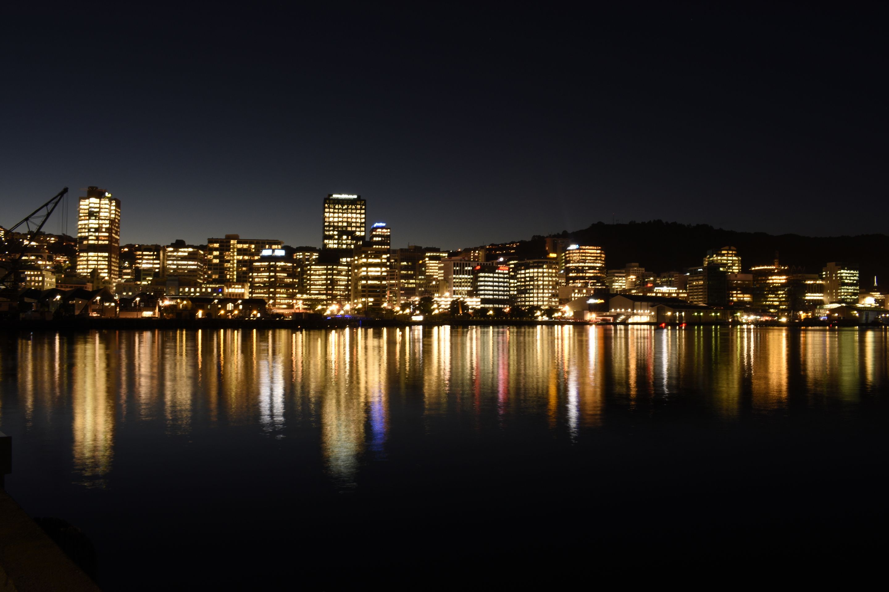 A stunning view of Wellington city illuminated at night with reflections on water, showcasing urban architecture.