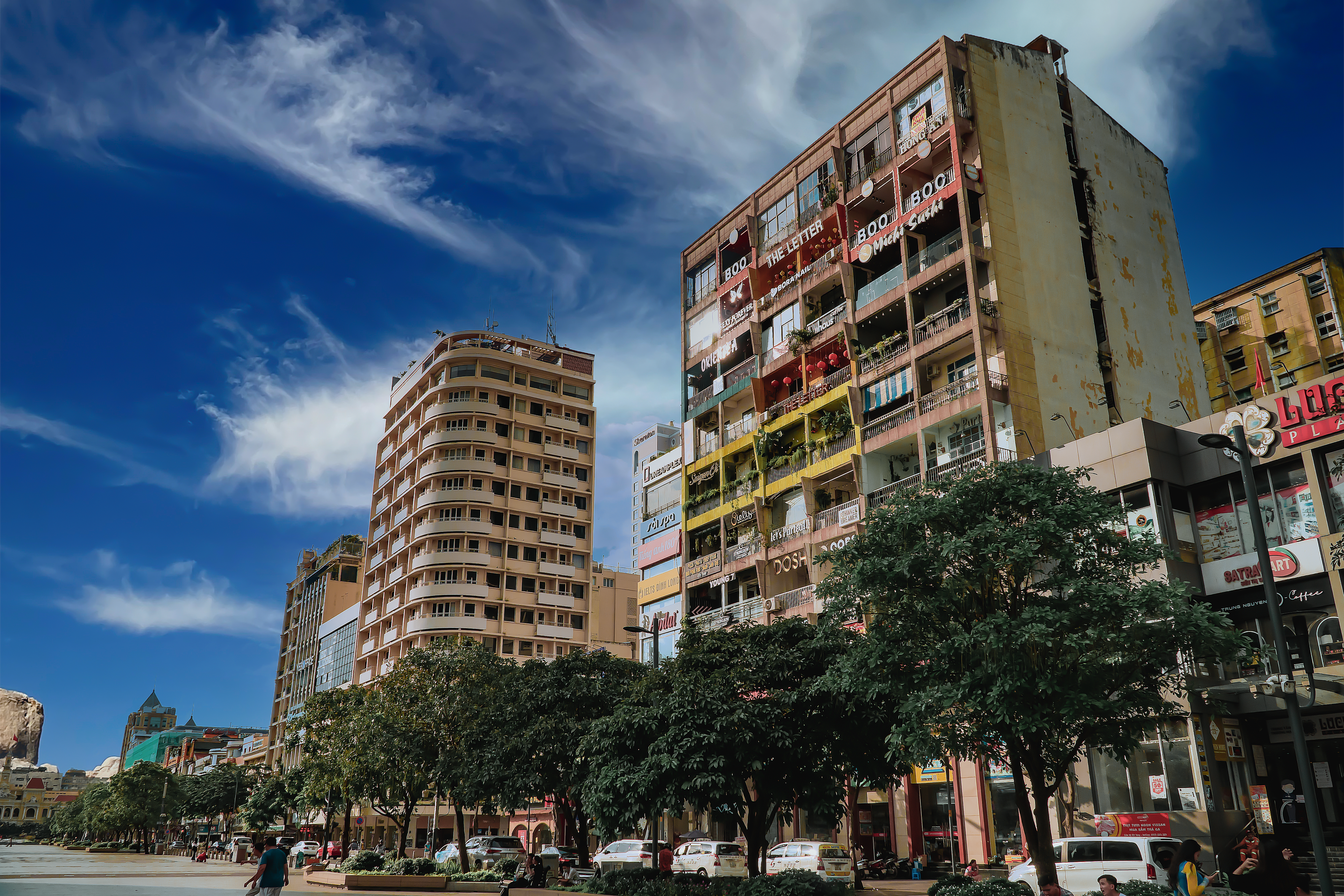 Cityscape view featuring tall buildings, trees, and a vibrant blue sky.